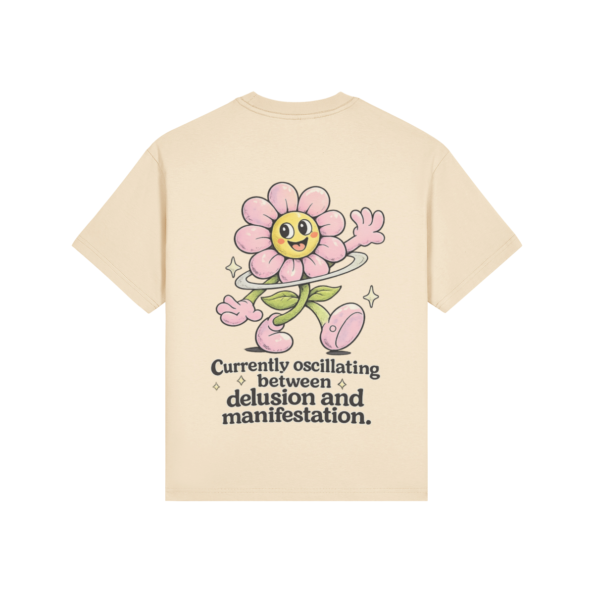 Back view of a cream-colored t-shirt featuring a large retro cartoon pink flower character with a hula hoop, sparkles, and the text “Currently oscillating between delusion and manifestation” in bold black lettering.